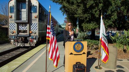 Asm. Irwin at podium, speaking, with train in background
