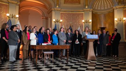 Asm. Irwin at podium, speaking, while fellow legislators listen on