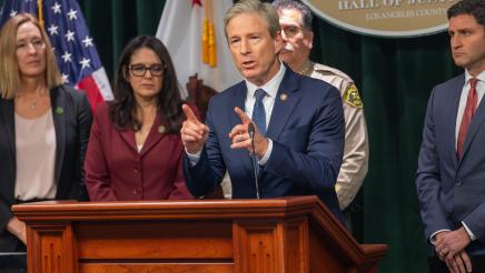 Asm. Irwin listens on as guest speaker stands at podium and speaks