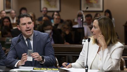 Asm. Irwin listen on as witness provides testimony while holding up vape box